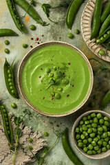 Green pea puree soup decorated microgreens in a beige ceramic bowl. On the background of the canvas ceramic dishes with pods and grains of peas. Top view. Flat lay food
