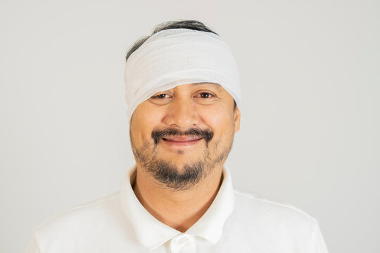 Close-up portrait of smiling Asian man with bandage on his head over white background.