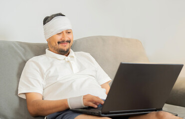 Handsome cheerful man with a broken wrist and head in bandage sitting and working at home.
