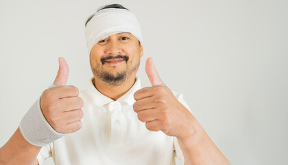 Handsome Asian man injured for accident wearing bandage and strips on head doing happy thumbs up gesture with hand.