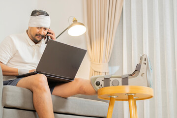 Happy recovery man from accident fracture broken bone injury with leg and head, support wrist while work with laptop