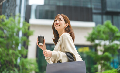 Single adult asian woman holding take away coffee cup and shopping bag on black friday sale city...