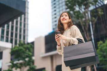 Single adult asian business woman holding take away coffee cup and shopping bag on black friday...