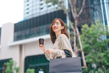 Single adult asian business woman holding take away coffee cup and shopping bag on black friday...