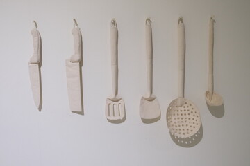 A set of kitchen utensils made from soft white fabric hangs neatly on a wall, resembling knives and...