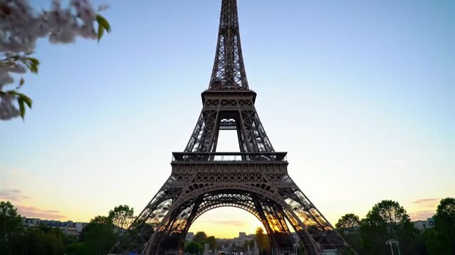 The Eiffel Tower rises against a clear sky, framed by trees and blossoms, showcasing its iconic architecture.