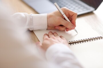 Man writing in notepad with pen at wooden table, closeup