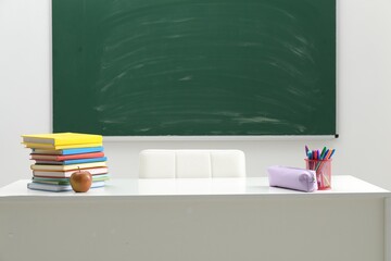 Different school stationery and apple on white table near blackboard indoors