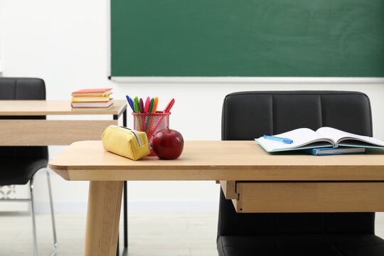 Different school stationery and red apple on wooden table near blackboard indoors