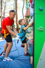 little three year old boy persistently climbs a climbing wall with a safety harness