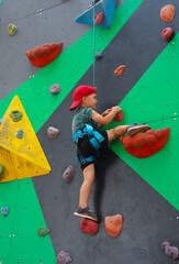 little three year old boy persistently climbs a climbing wall with a safety harness