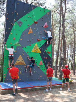 Teenagers climb a climbing wall using holds secured with ropes at a scout camp