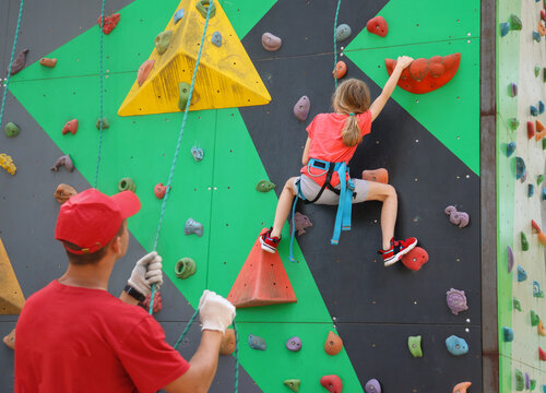 Teenagers climb a climbing wall using holds secured with ropes at a scout camp
