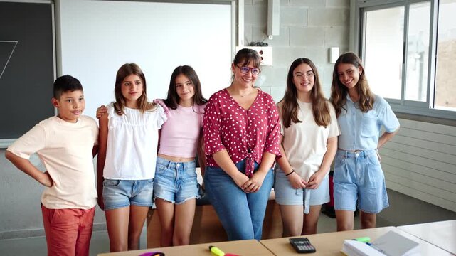Happy junior school students children group looking at camera standing in classroom with female teacher