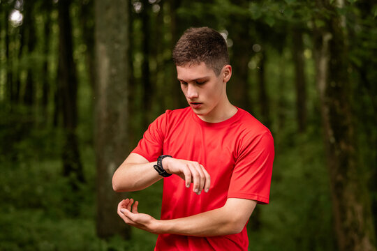 Young man in red t-shirt checking his fitness tracker in a forest