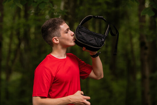 Young man in red shirt drinking from water bottle in black hip pack