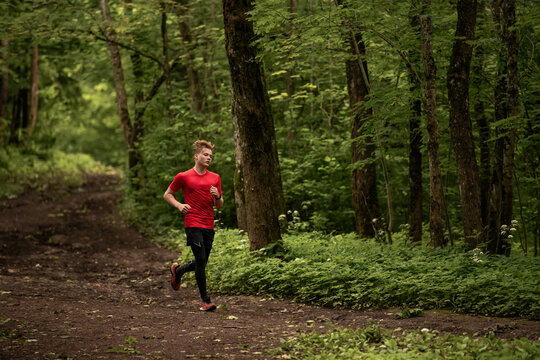 Young caucasian man running through green summer forest park.