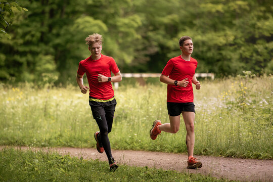 Two teenage boys running along a path in a park