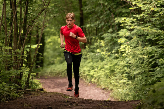 Young caucasian man running through green summer forest park.
