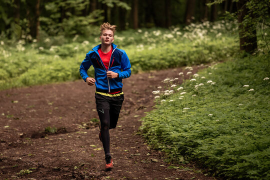 Young caucasian man running through green summer forest park.