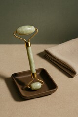 Jade roller on a stand. The jade roller has a green stone and a gold handle, next to it a towel