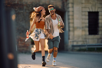 Cheerful man and his girlfriend holding hands while going to summer music festival.