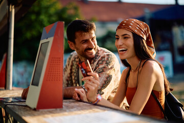 Cheerful couple using payment card while buying drinks at summer music festival.