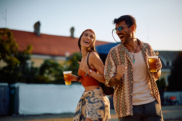 Cheerful couple drinking beer and dancing at open air music festival in summer.