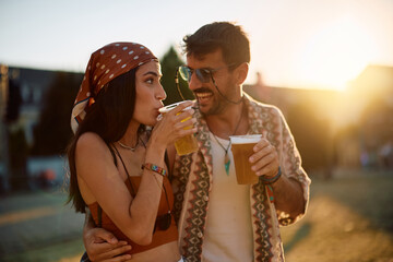 Happy couple of festival goers drinking during music concert in summer.