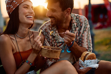 Close up of happy couple of festival goers enjoying in food at sunset.