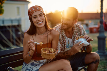 Happy couple eating fast food during open air music festival at sunset.
