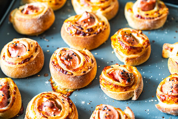 Sausage in dough, freshly baked mini rolls of puff pastry with cheese and sausage inside on a gray background.