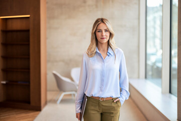 Confident blond businesswoman with hand in pocket at office