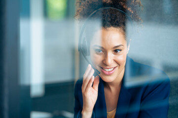 Smiling businesswoman listening through headset in soundproof cabin