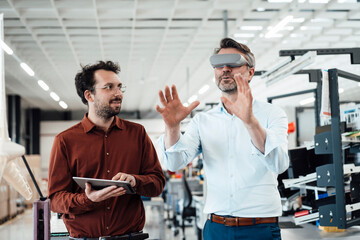 Businessman with colleague wearing virtual reality simulator gesturing at industry