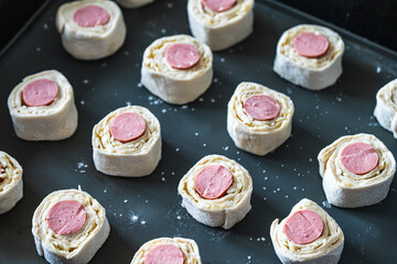 Sausages wrapped in raw puff pastry on a baking mat, ready to bake in the oven.