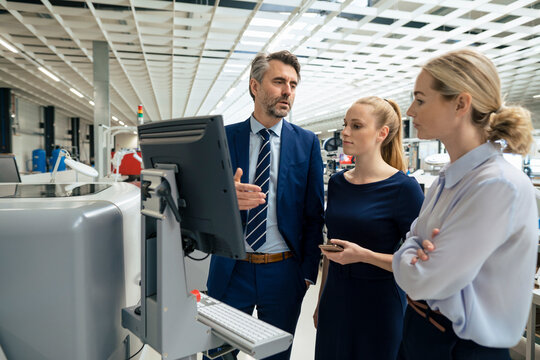 Mature businessman having discussion with colleagues over desktop computer in industry