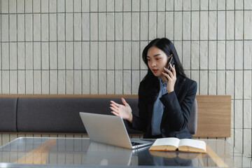 Businesswoman talking on phone and working on laptop in modern office
