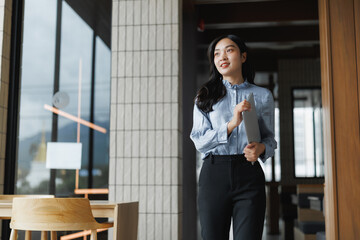 Young asian businesswoman walking through modern office holding tablet computer