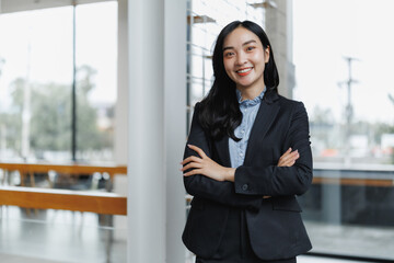 Smiling asian businesswoman standing with arms crossed in modern office