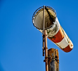 Orange and white windsock indicating wind direction, attached to a rusty metal pole against a clear...