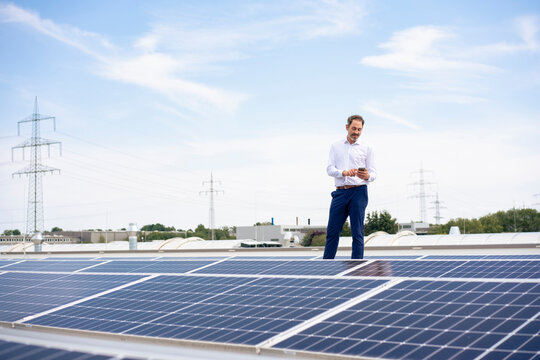 Businessman using smart phone standing by solar panels on rooftop