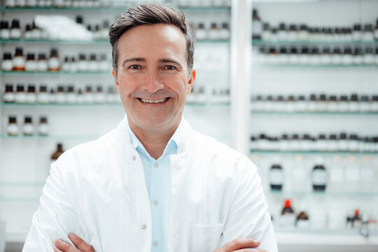 Happy pharmacist in front of medicines on shelf at store