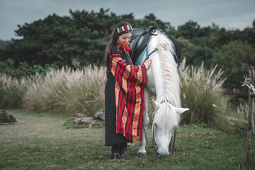 Woman in Traditional Attire Petting a White Horse in Pastoral Setting
