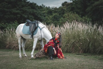 Elegant Woman in Traditional Attire Sitting by Beautiful White Horse