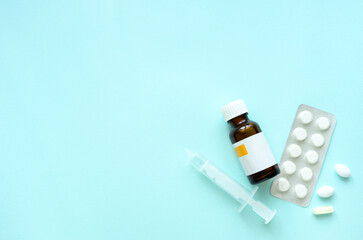 Medical syringe, white pill blister packs, and brown medicine bottle on blue background. Clean and...