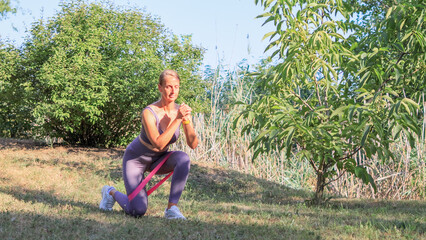 Fit Woman Doing Squats with Resistance Band Outdoors in Nature