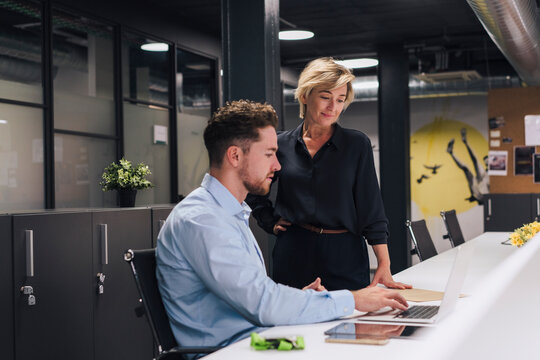 Young businessman explaining colleague over laptop in office