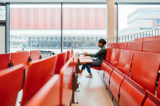 Young woman working on tablet PC sitting on seat in auditorium