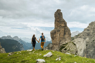 Iconic friulan mountain Campanile Di Val Montanaia, Dolomiti Friulane, Val Cimoliana, Cimolais Friuli Venezia Giulia, Italy. A couple with backpacks holds hands, gazing at the mountain view.